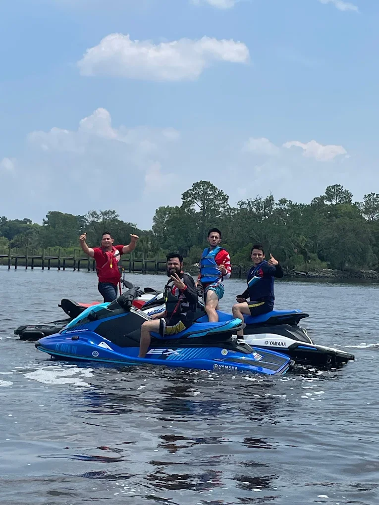 Four men riding Yamaha jet skis on a body of water with trees in the background and partly cloudy sky.