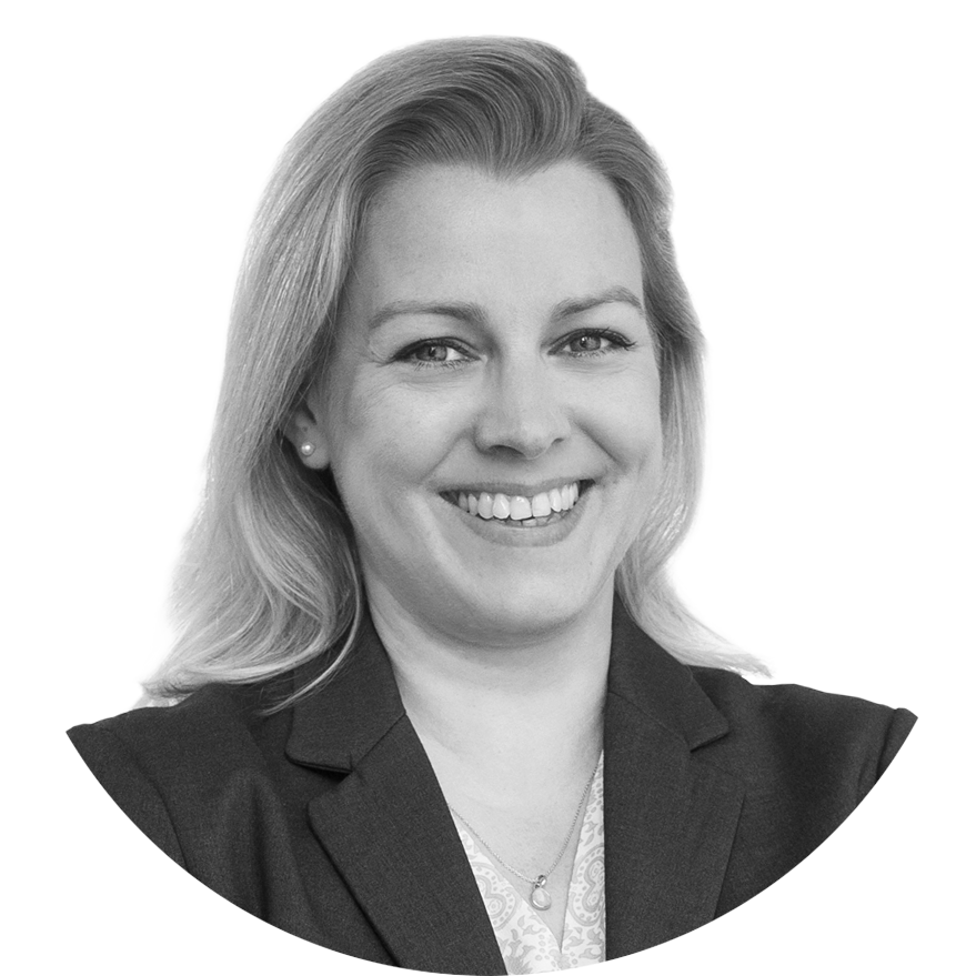 Black and white professional portrait of a woman smiling, with blonde hair, wearing a blazer and a necklace.