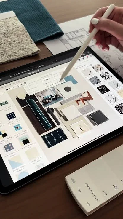 Person using a stylus on a tablet to browse interior design or decor images on a digital mood board or catalog, with fabric samples nearby.