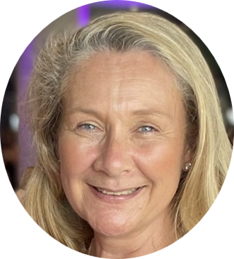 Close-up of a smiling middle-aged woman with blonde hair, wearing a purple top and earrings, in front of a blurred purple background.