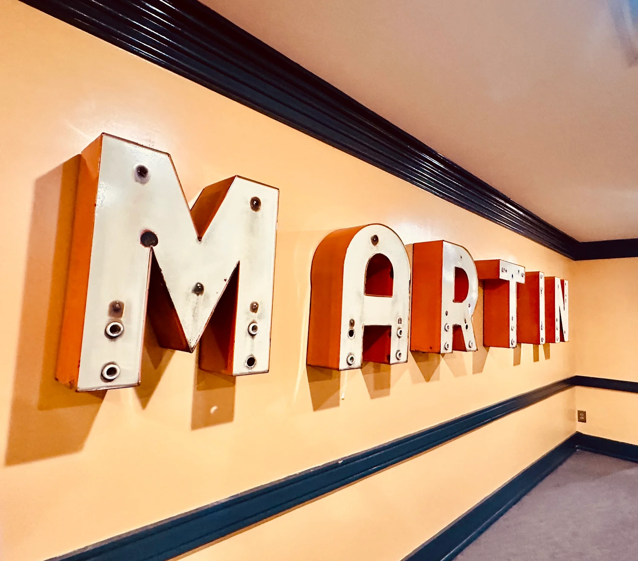 Large decorative letter sign spelling 'MARTIN' on a yellow wall, with each letter illuminated by light bulbs.