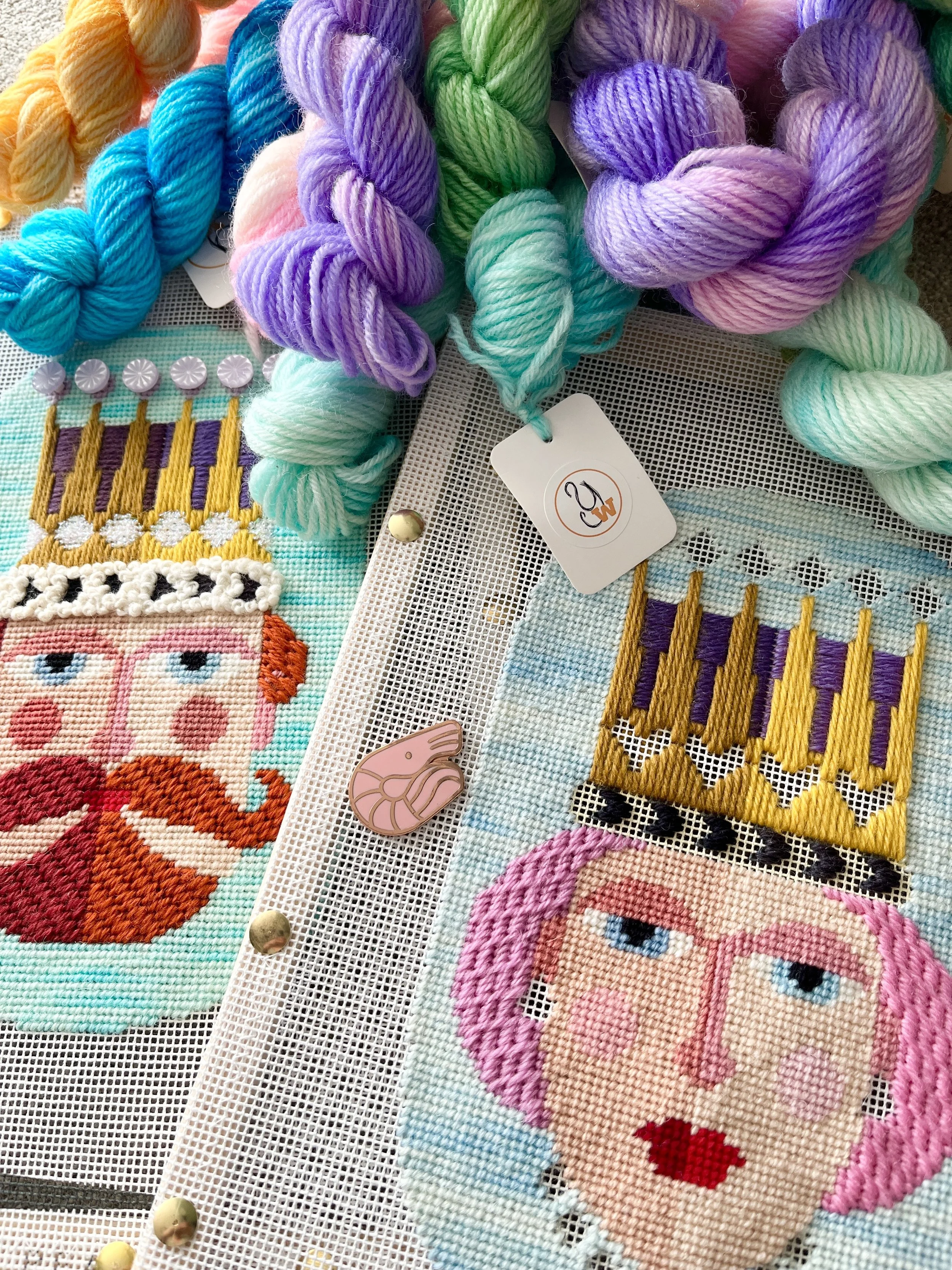 Close-up of colorful embroidered fabric and bundles of pastel-colored embroidery floss on a white mesh backing.