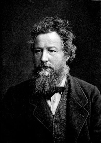 A black and white portrait of a man with a full beard and wavy hair, wearing a dark coat.