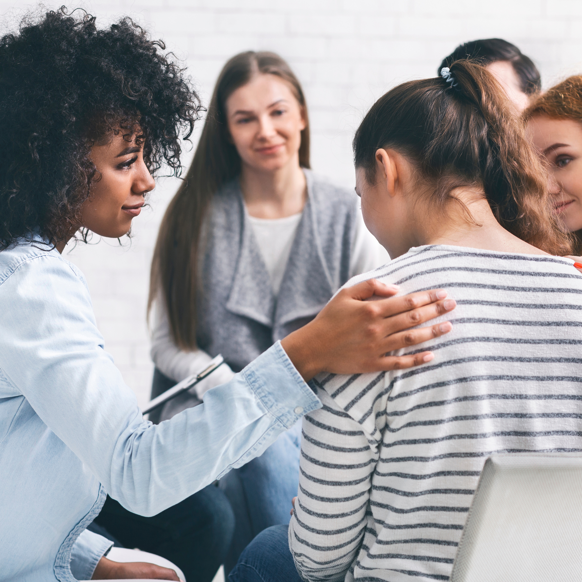 A group of diverse women in a circle, comforting each other, with one woman gently holding another's arm, indicating support and empathy.