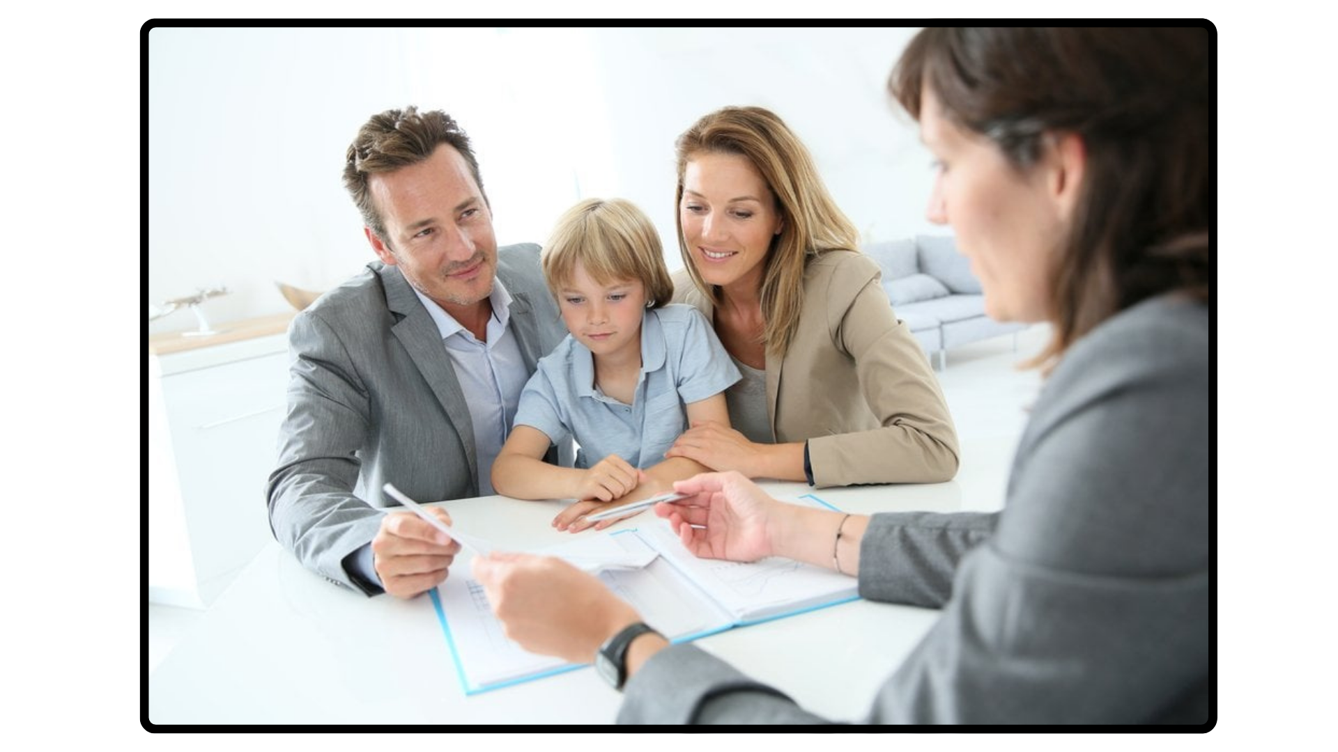 Family meeting with a woman, two adults, and a child sitting at a table, talking with a woman across from them who is holding papers.