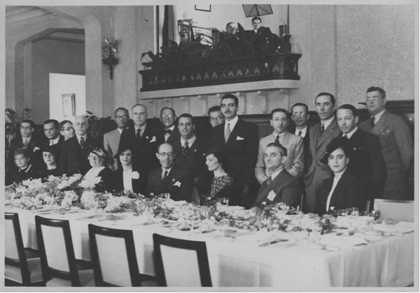 Mário de Andrade sentado ao centro, com Liddy Chiaffarelli Mignone de vestido estampado, ao seu lado.  Neste evento, realizado no final da década de 1930, também estavam presentes Antônio de Sá Pereira e Manuel Bandeira. Acervo Fotográfico do Conserv