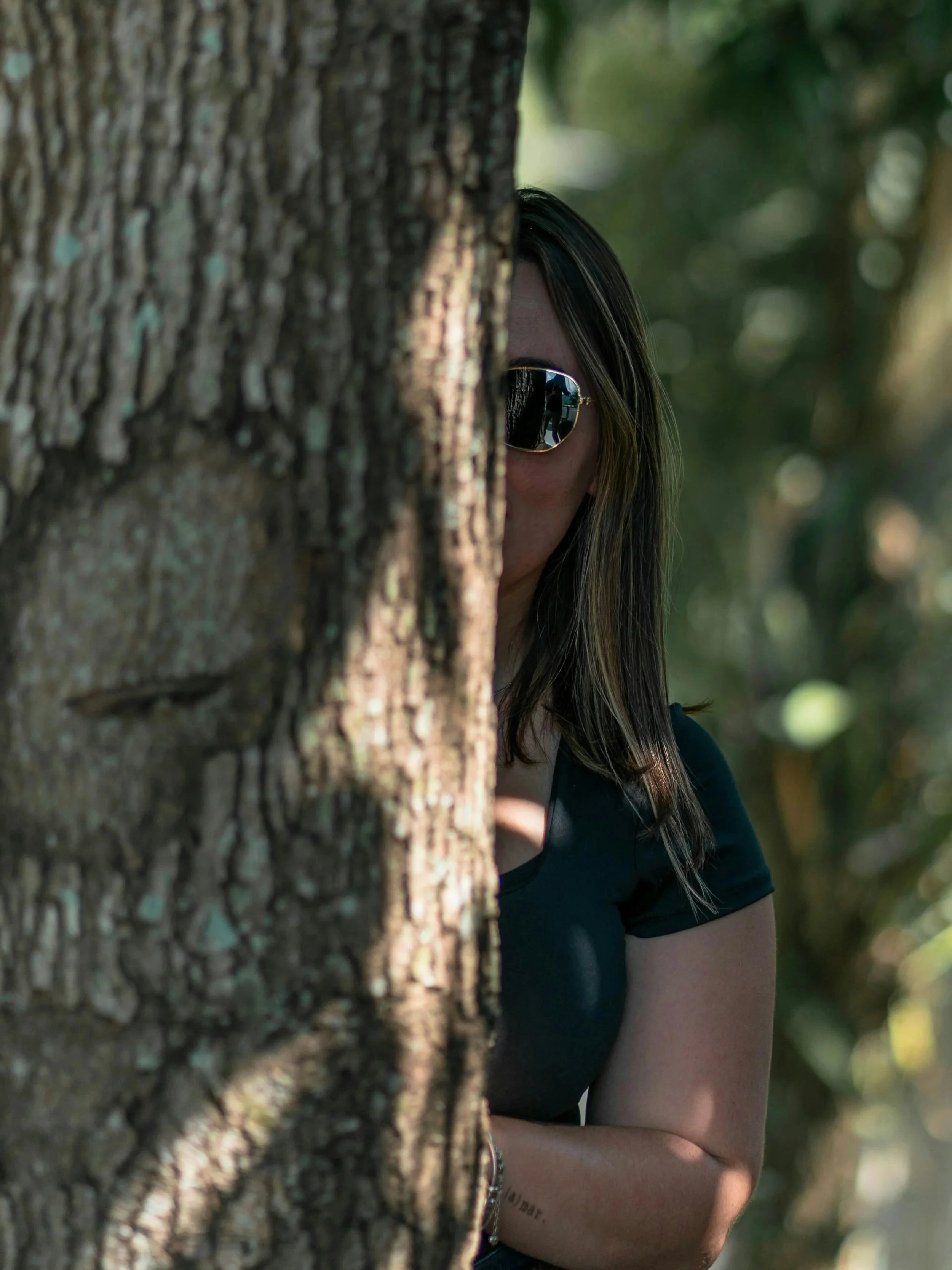 Woman in sunglasses hiding behind tree