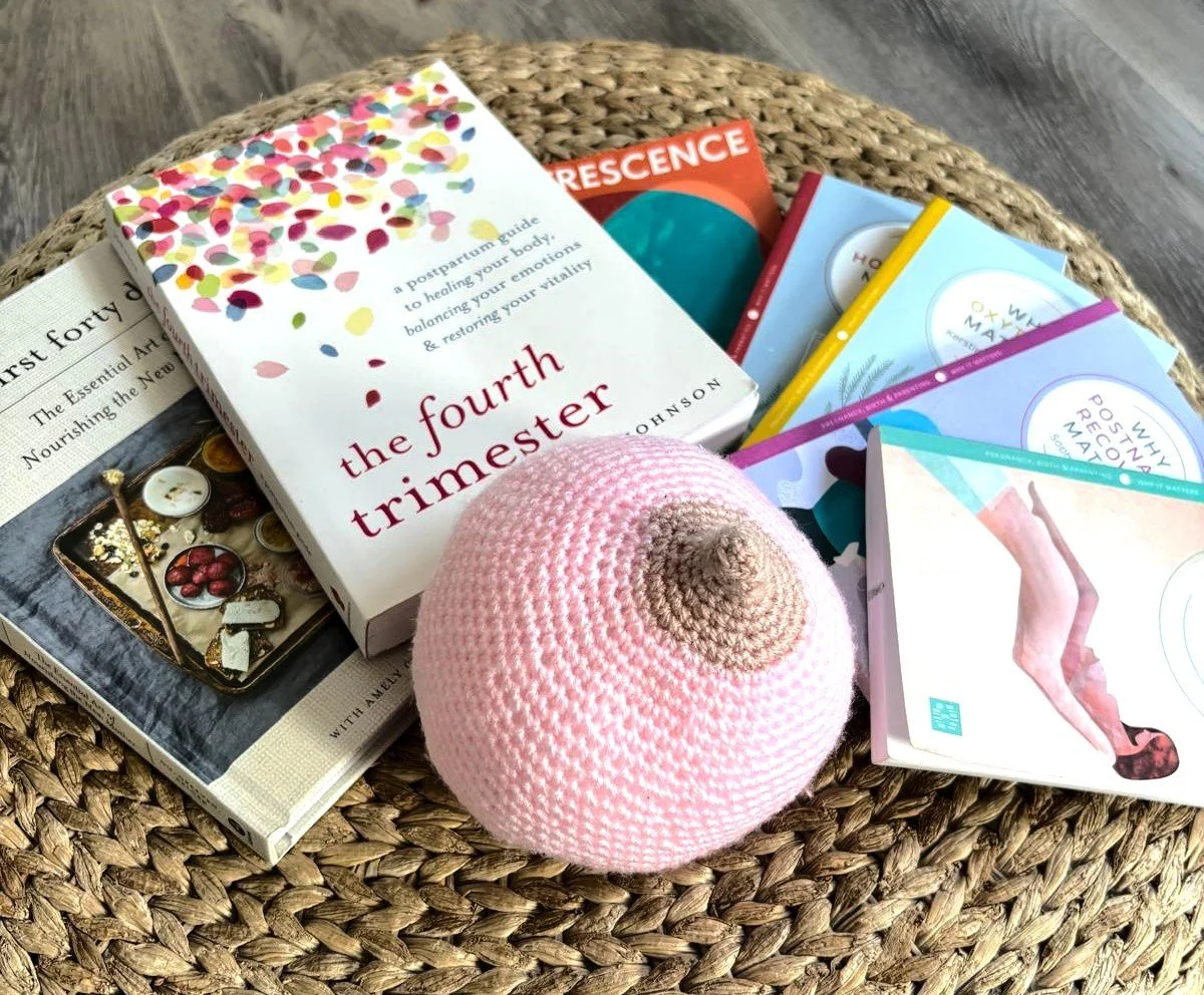 A wicker table with books, a pink knitted hat, and a newspaper, on a wooden floor.