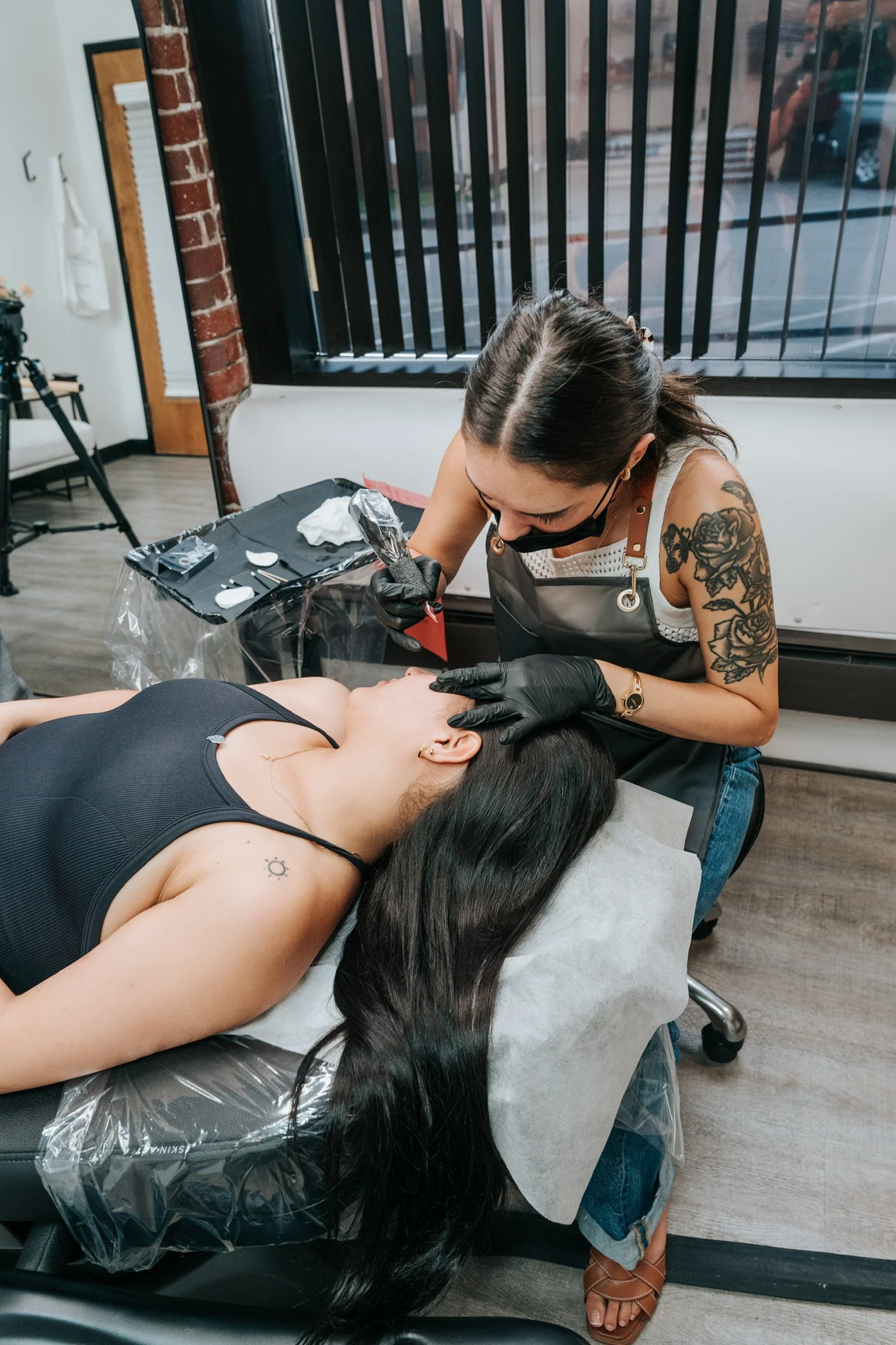 Tattoo artist is giving a tattoo to a woman lying on a tattoo bed in a tattoo studio.