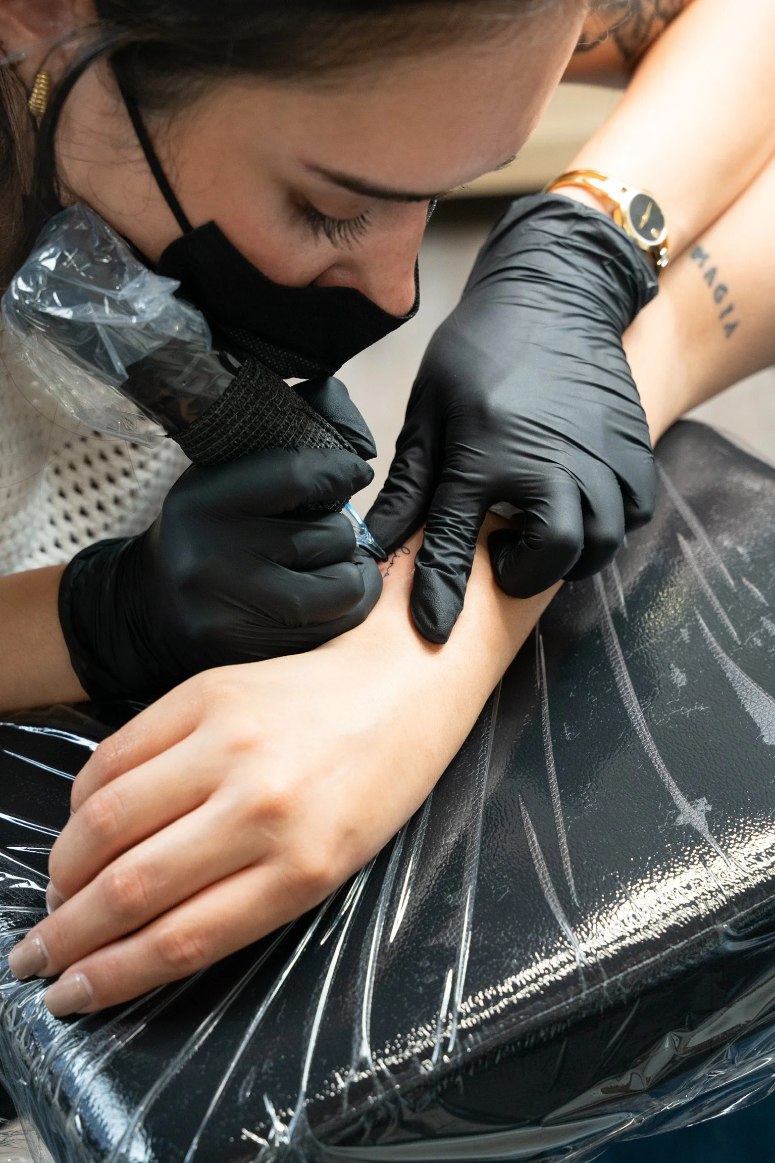 Tattoo artist using a tattoo machine on a person's forearm.
