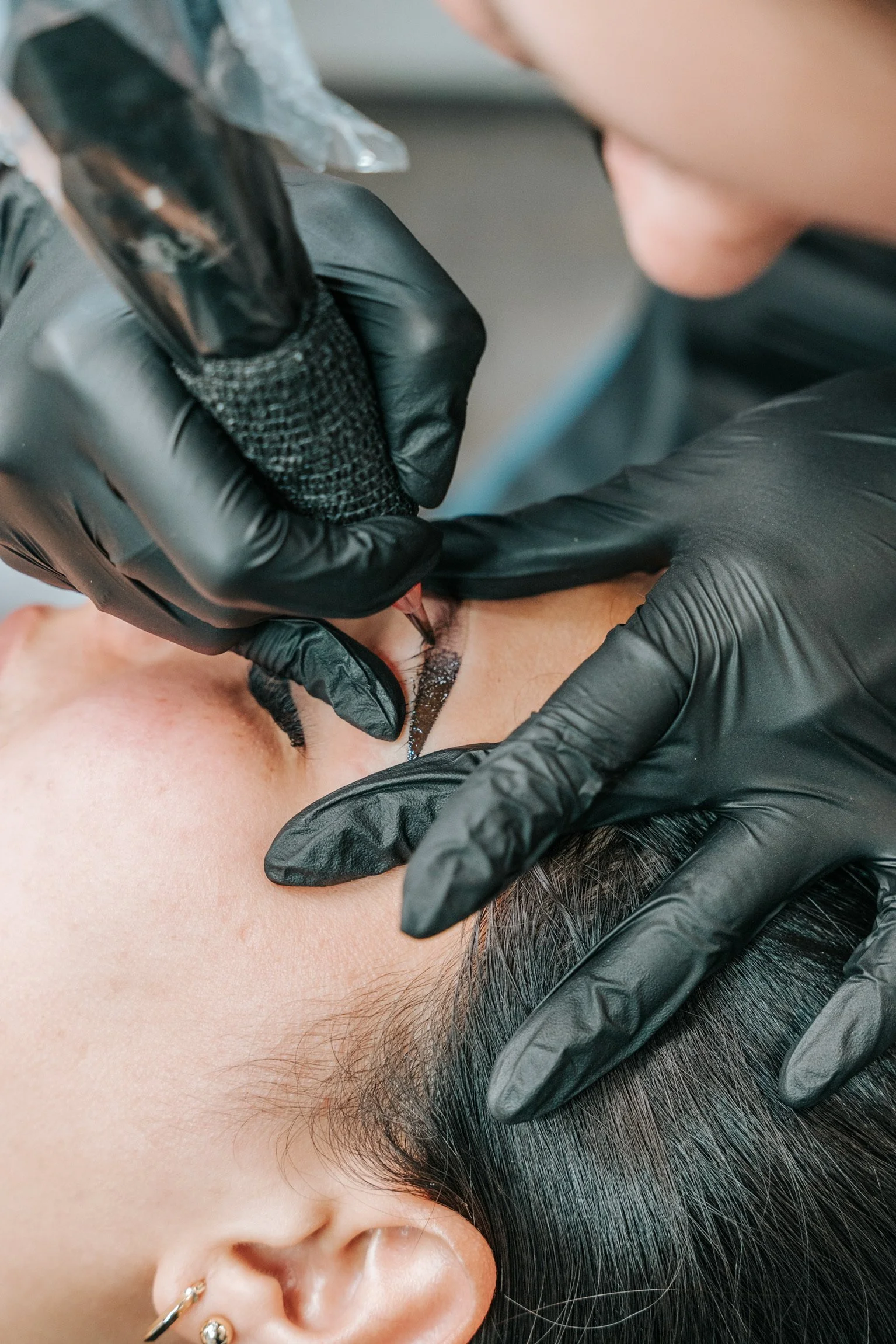 A person receiving a tattoo on their forehead from an artist wearing black gloves.