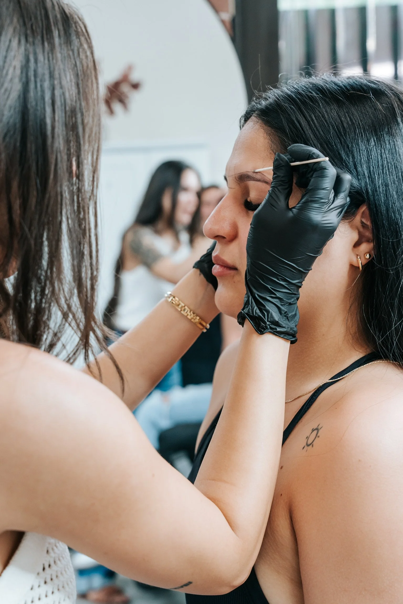 A woman receiving a cosmetic tattoo or microblading procedure on her eyebrows from a professional artist in a beauty salon.