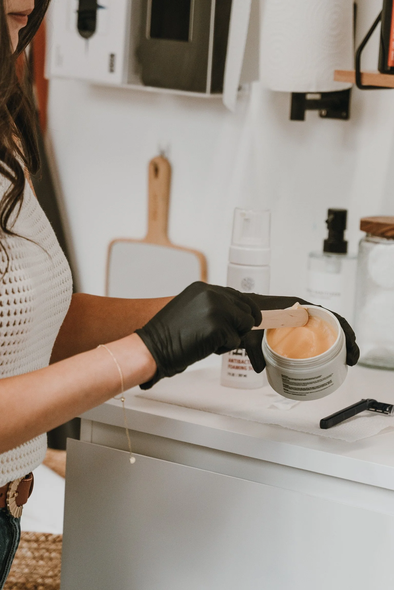 Person wearing black gloves scooping a peach-colored substance from a jar into a spatula in a kitchen.