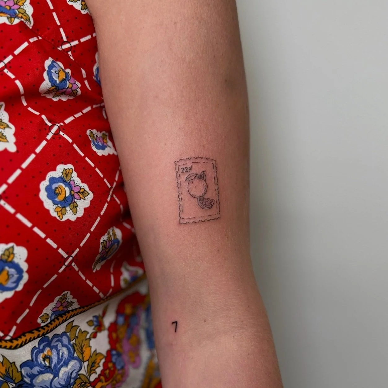 Tattoo of a postage stamp featuring a peach and the number 22, on a person's forearm.