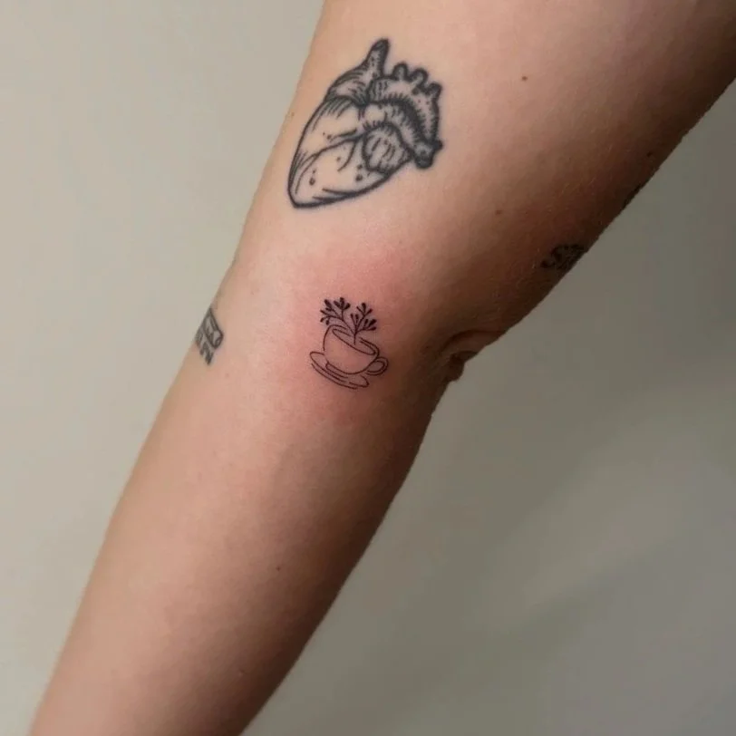 Tattoo of a human heart and a cup with herbs on a person's arm.