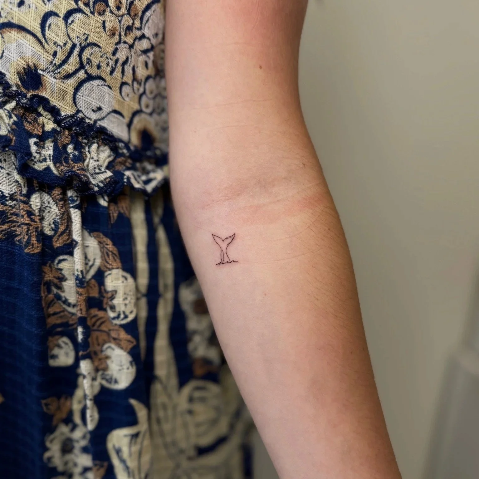 Close-up of a person's arm showing a small tattoo of a whale's tail on the inner forearm.