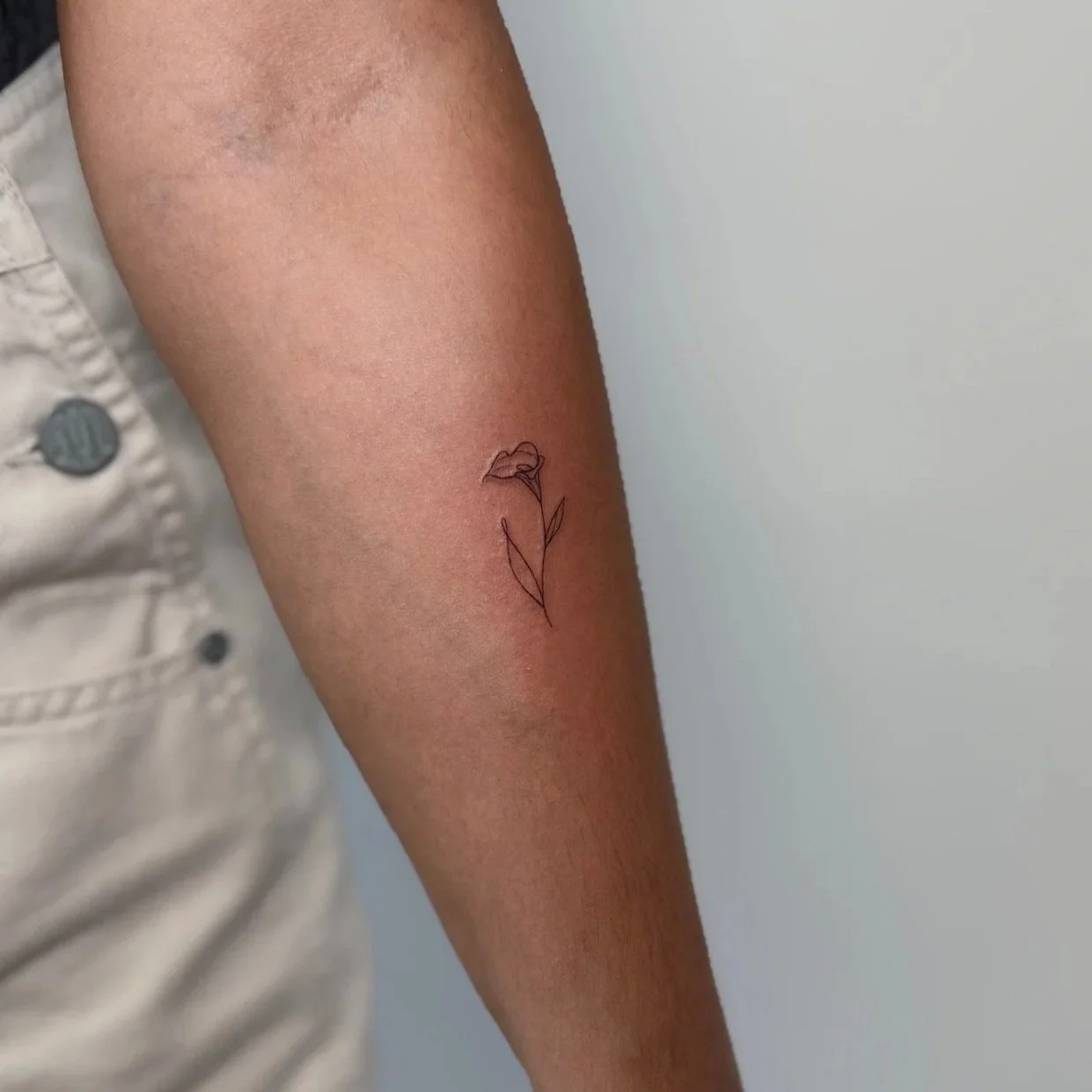 A person's inner forearm with a small minimalist tattoo of a flower sketch in black ink.
