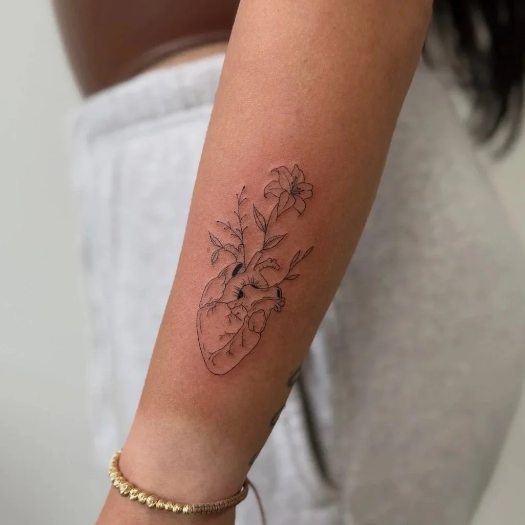 Tattoo of a heart with flowers and leaves on a person's forearm.