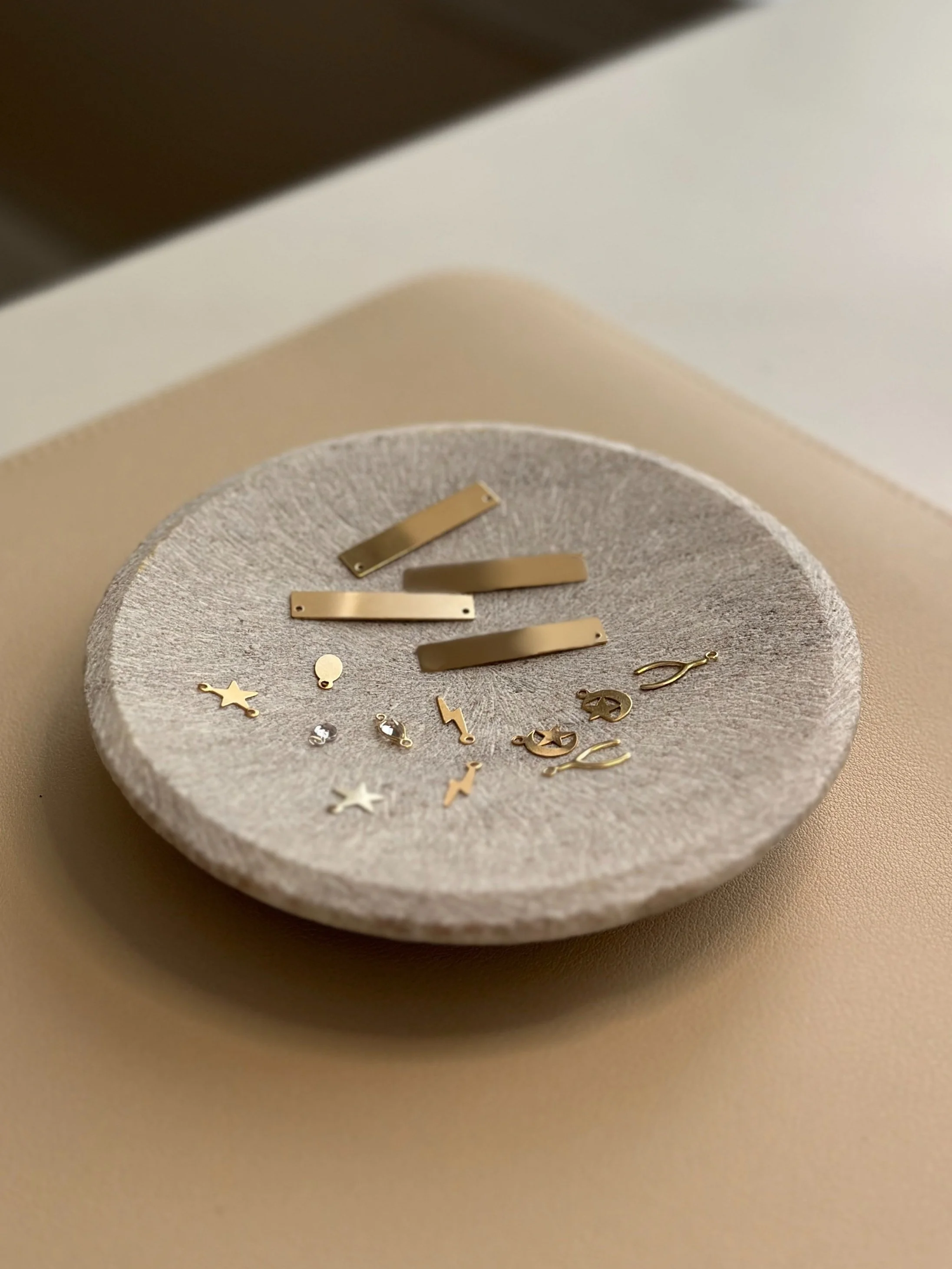 A circular stone dish containing various small gold jewelry pieces, including earrings, charms, and rectangular links.