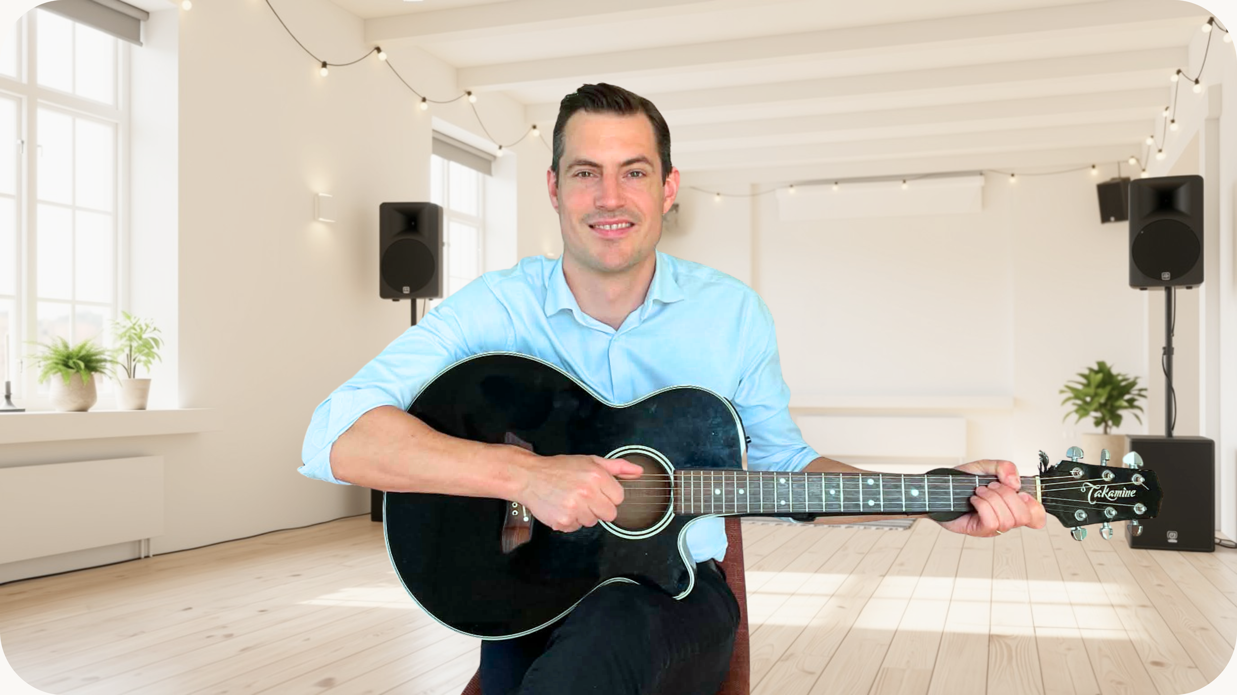 En mann som spiller akustisk gitar innendørs med lyse vegger, store vinduer, og planter.