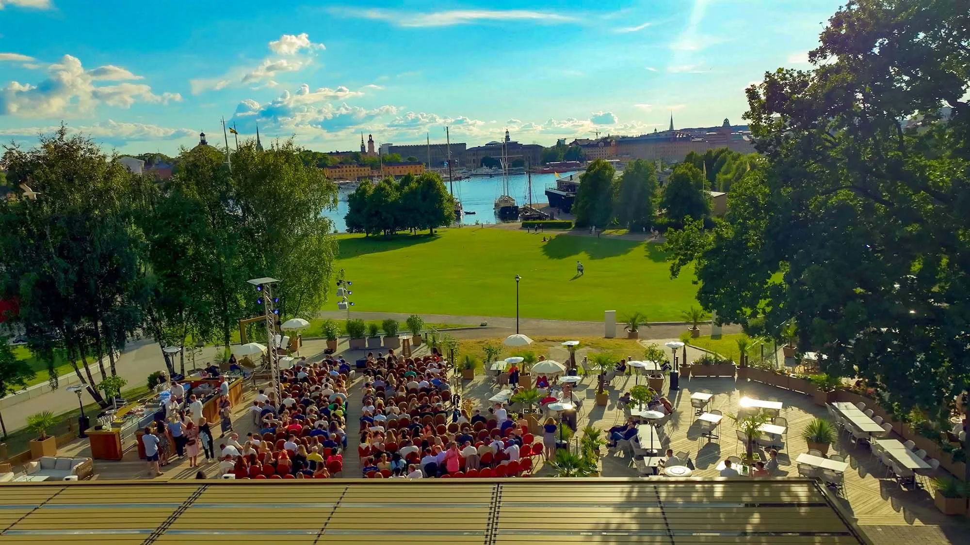Flygbild över Pergolan och eventarenan vatten och kungliga slottet i bakgrunden, samt båtar och stadssilhuett.