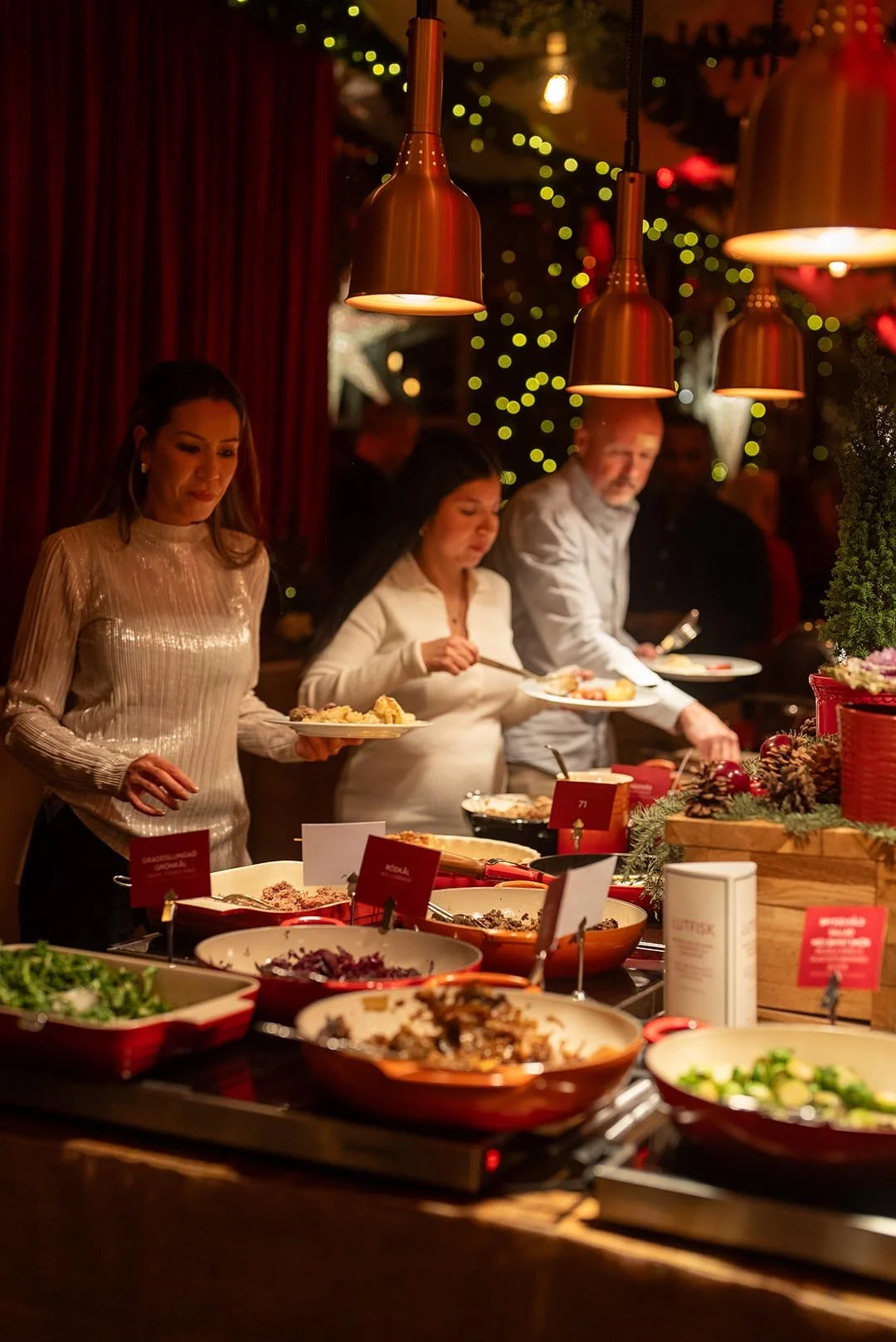 Personer som serverar julmat vid en buffé i en juldekorerad lokal.