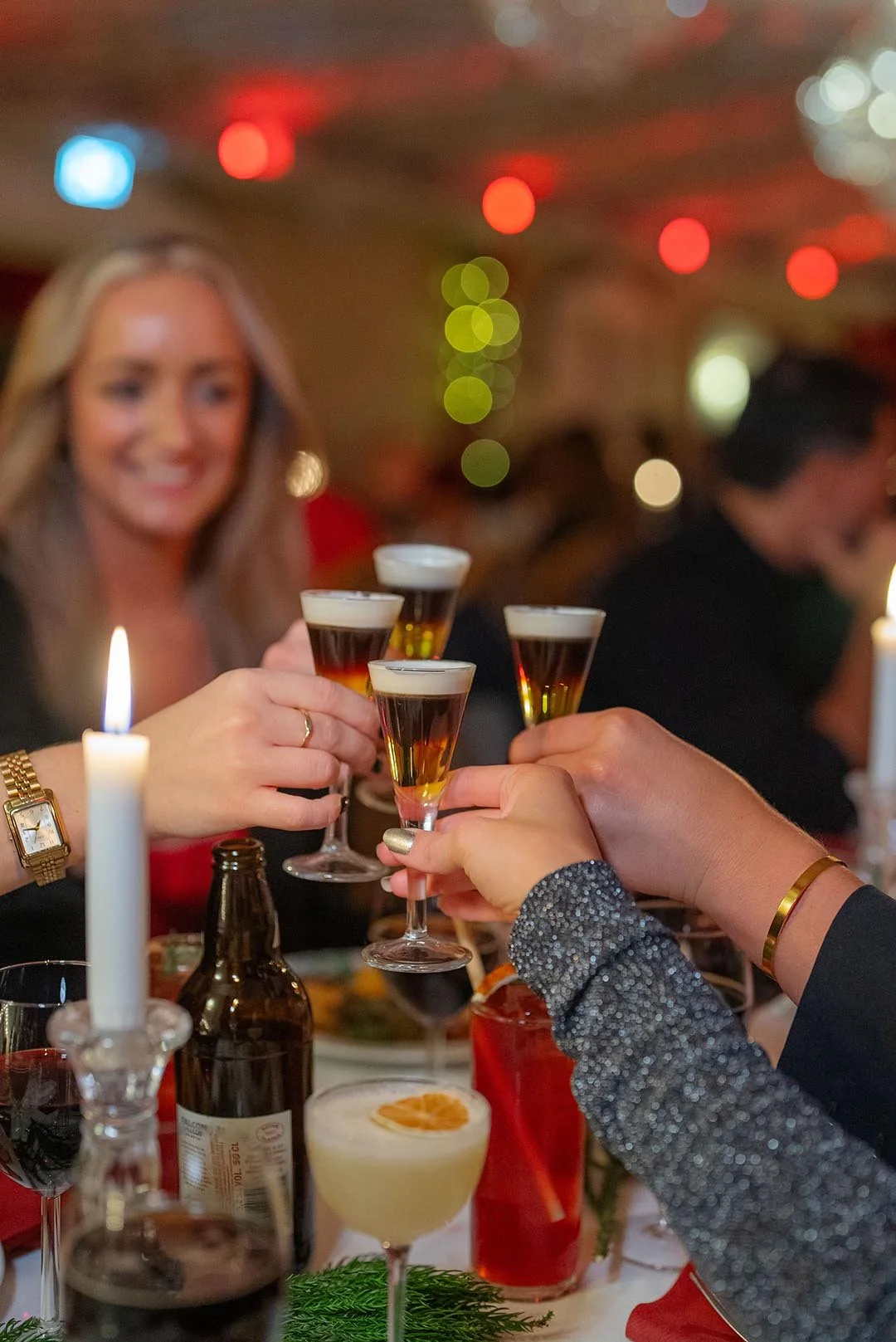 Folk som toasting med små drinkar på ett festligt bord med ljus och dekorationer.