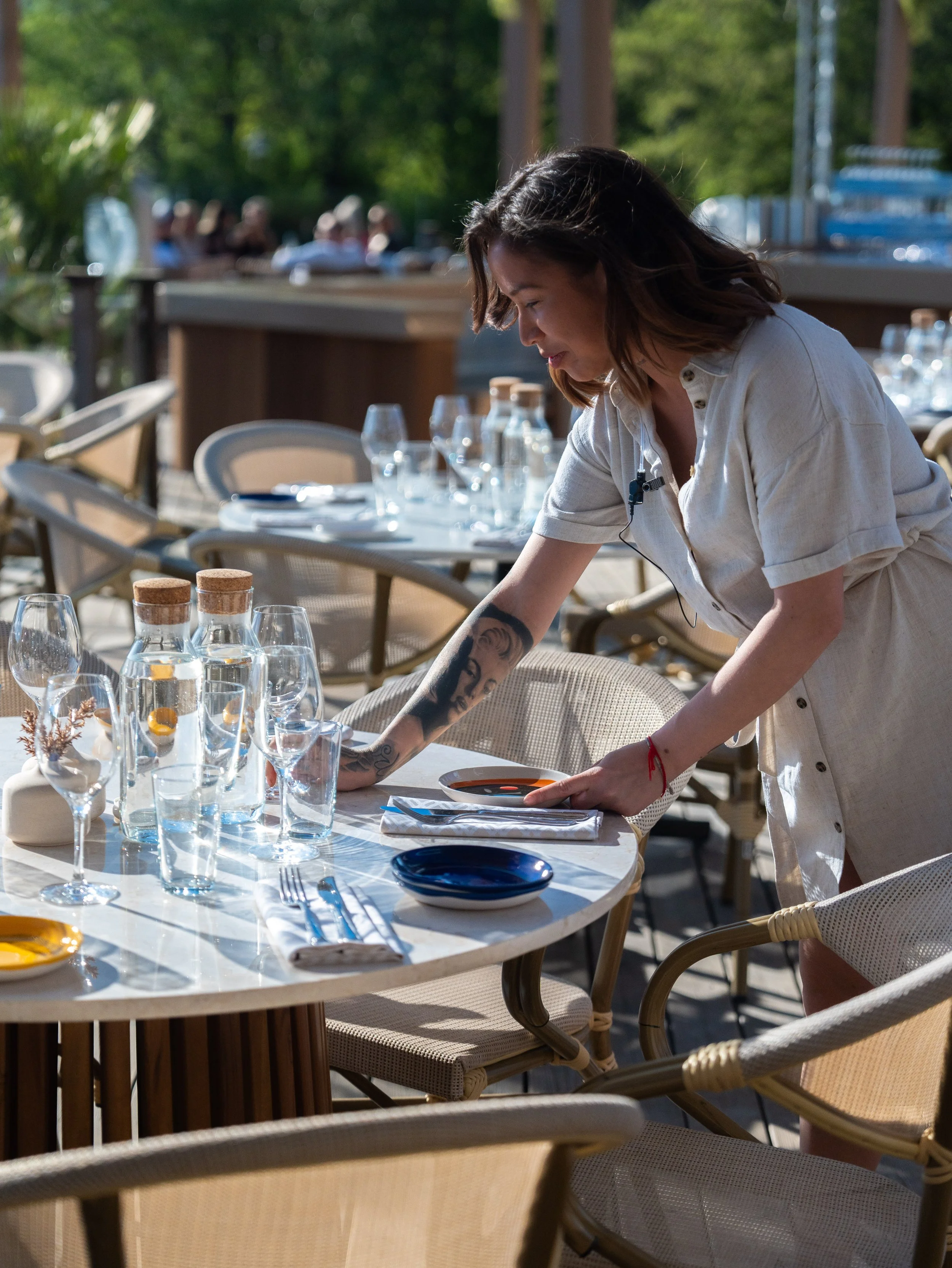 En servitör som ställer upp glas och tallrikar på ett utebord på en restaurang.