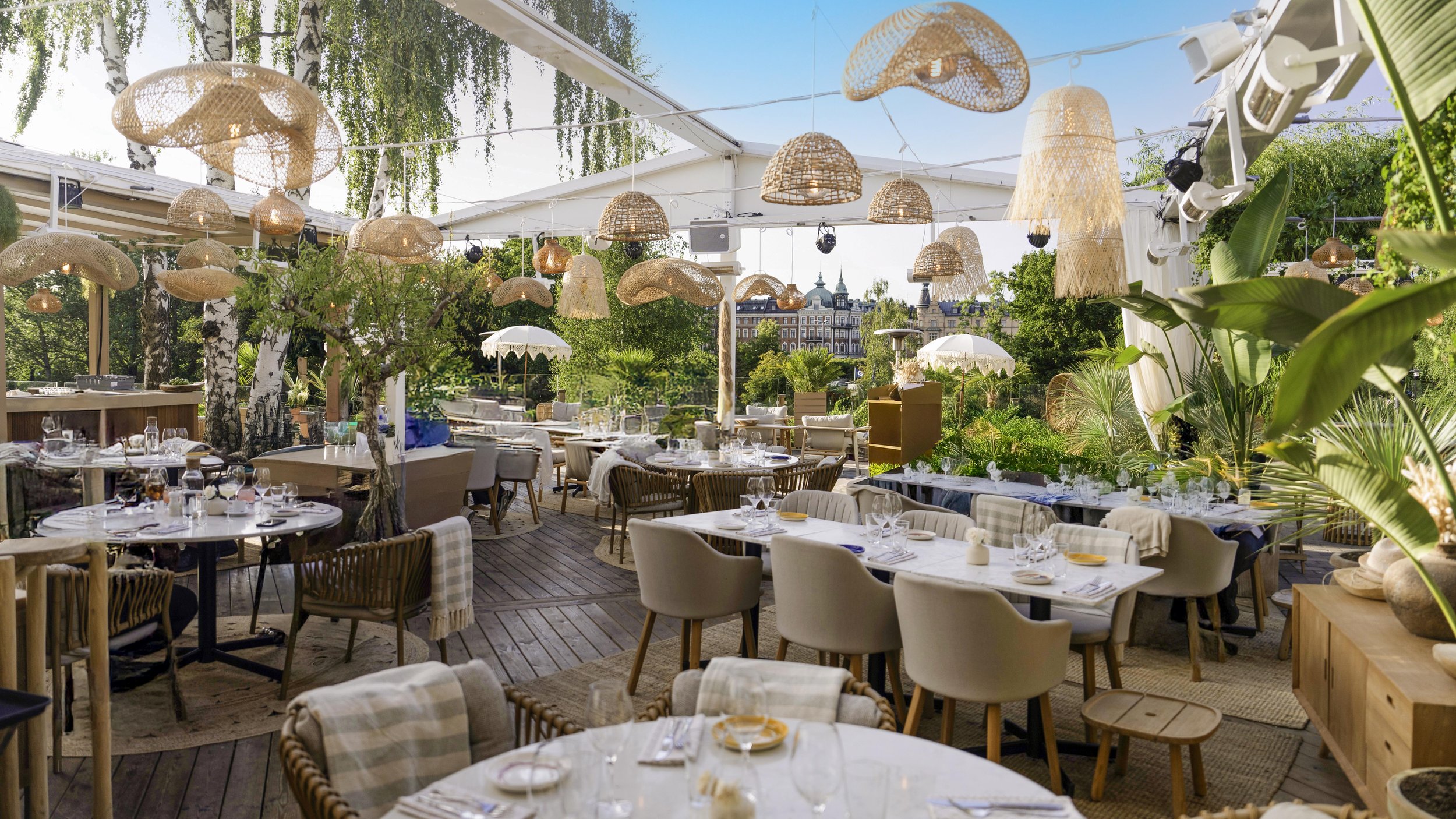 Upsett restaurang under bar himmel med utdragen bordsdukningar, gröna växter och hängande lampor