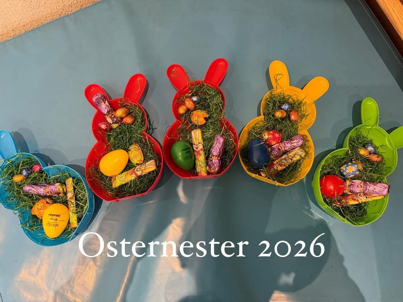 Colorful bunny-shaped baskets filled with decorated Easter eggs and grass, with the caption "Osternester 2026"