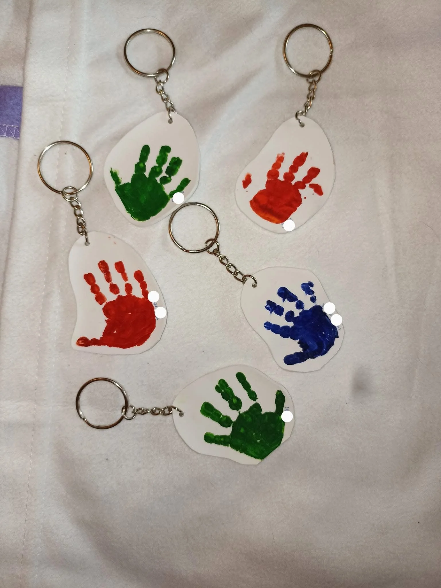 Five keychains featuring colorful handprints in green, red, and blue paint on transparent acrylic tags, with metal rings and chains.