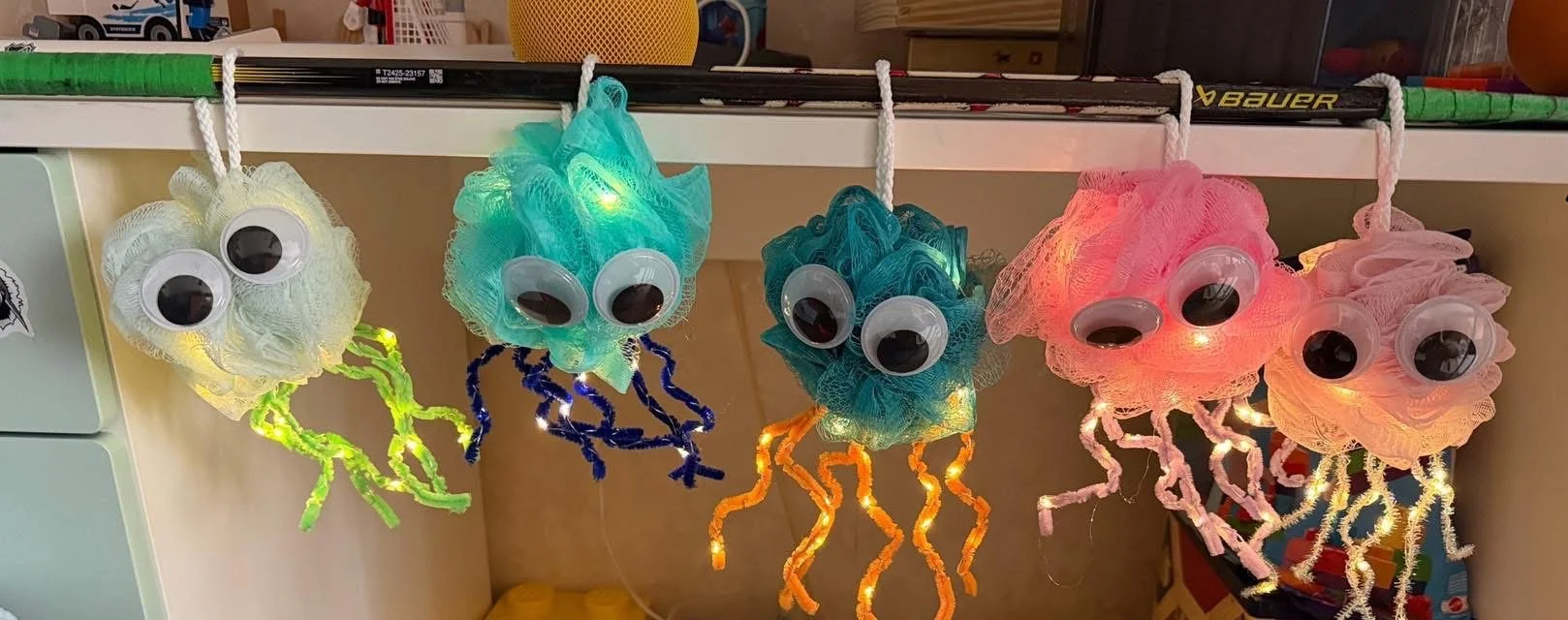 Colorful jellyfish-shaped light decorations hanging on a white shelf, each with googly eyes and illuminated tentacles in colors like yellow, green, blue, pink, and peach.