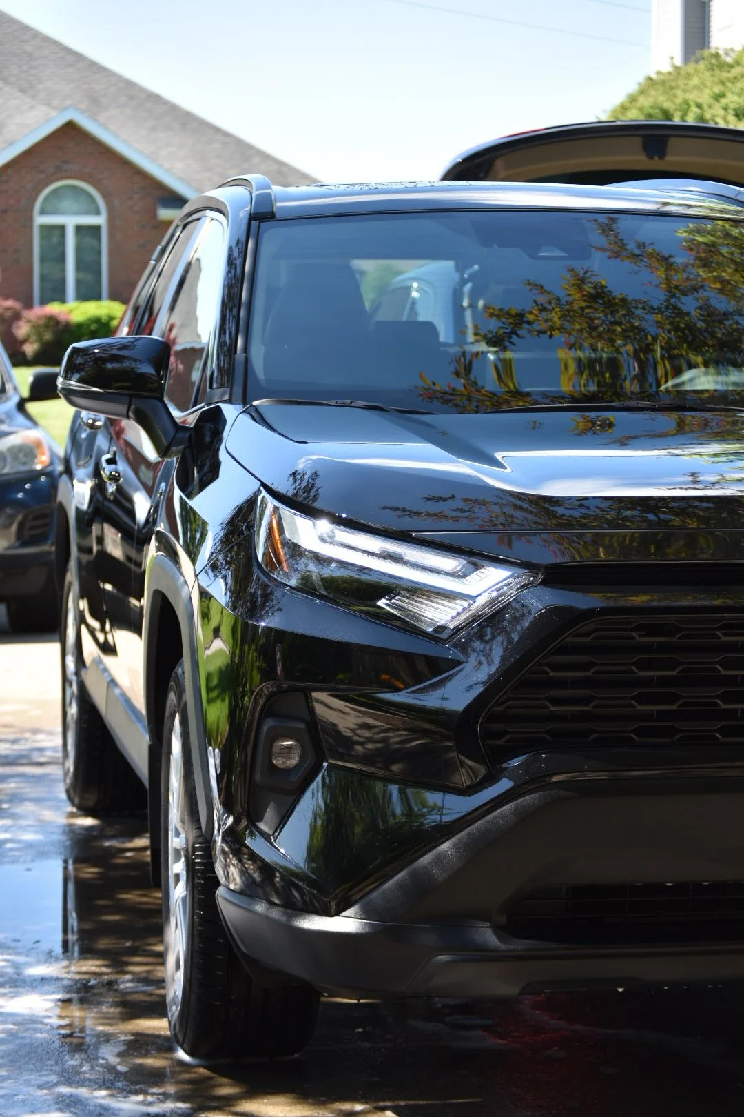 Close-up of a shiny black SUV parked in a driveway with a house and green trees in the background.