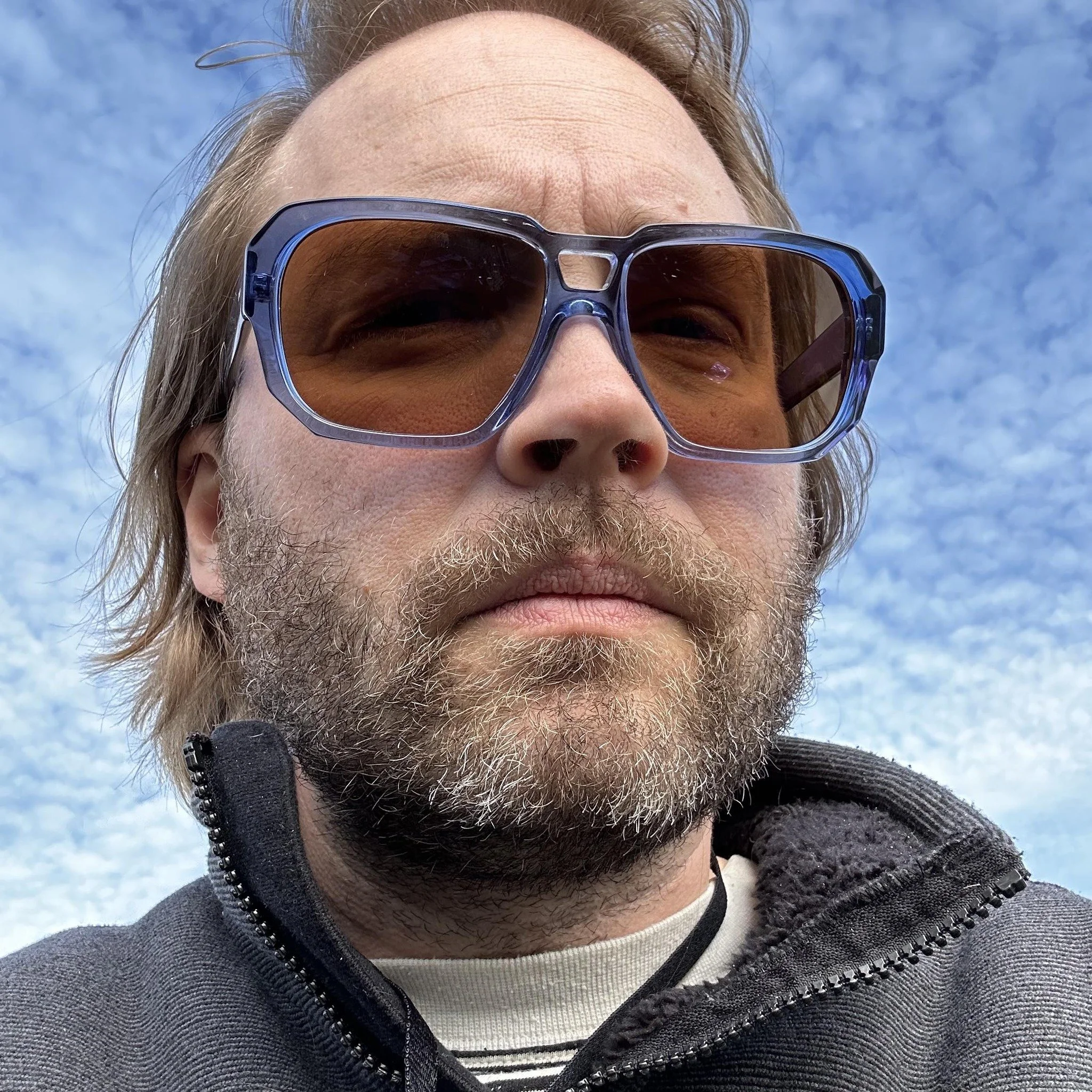 Close-up of a person's face wearing large sunglasses with a cloudy sky background.