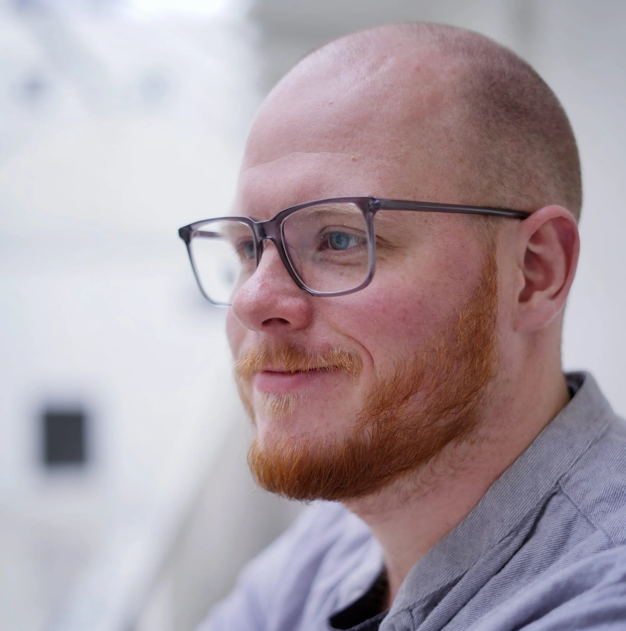 Close-up of a man with a shaved head, wearing glasses, and looking to the side.