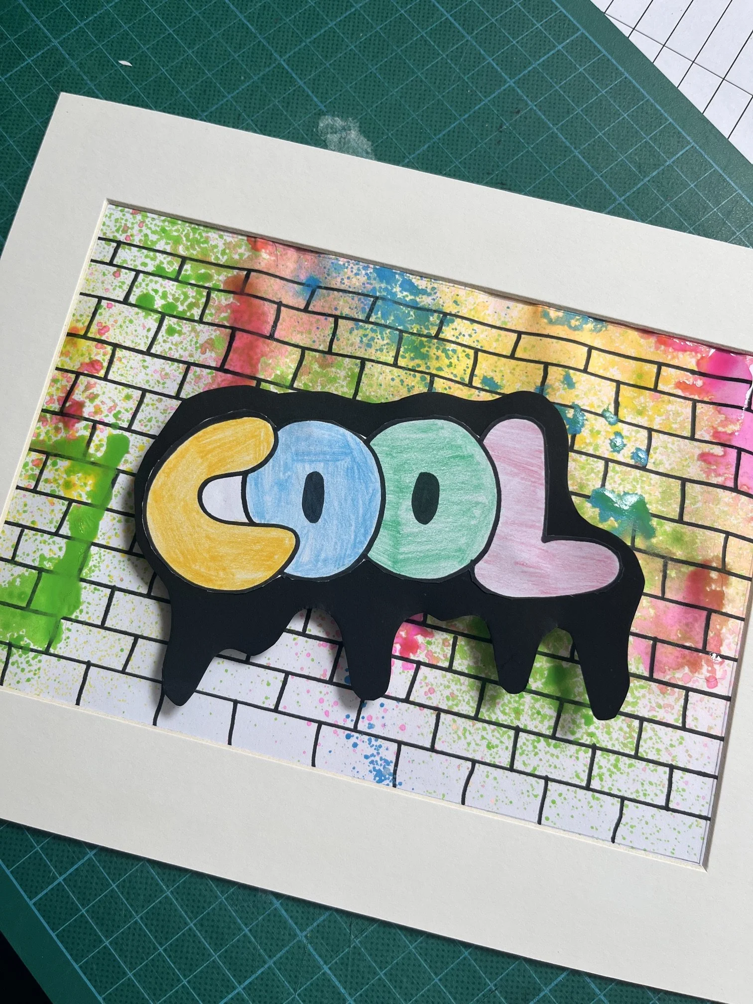 Close-up of colorful, abstract art with a background resembling a brick wall, with splashes of bright colors such as pink, blue, yellow, and green, and a black cutout with the word "SOO" written in colorful letters.