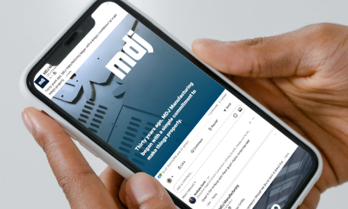 Person holding a smartphone displaying MDJ Manufacturing's LinkedIn page