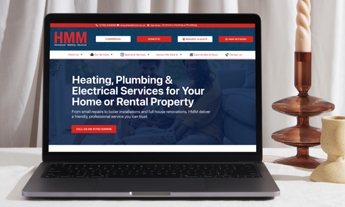 Laptop displaying a website for heating, plumbing, and electrical services on a desk with decorative items.