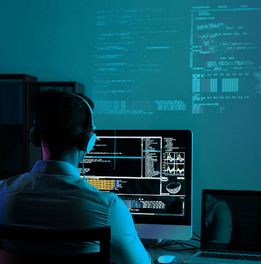 Personne assise devant un ordinateur avec un casque, travaillant sur du code informatique, dans une pièce sombre avec des projections de code à l'écran.