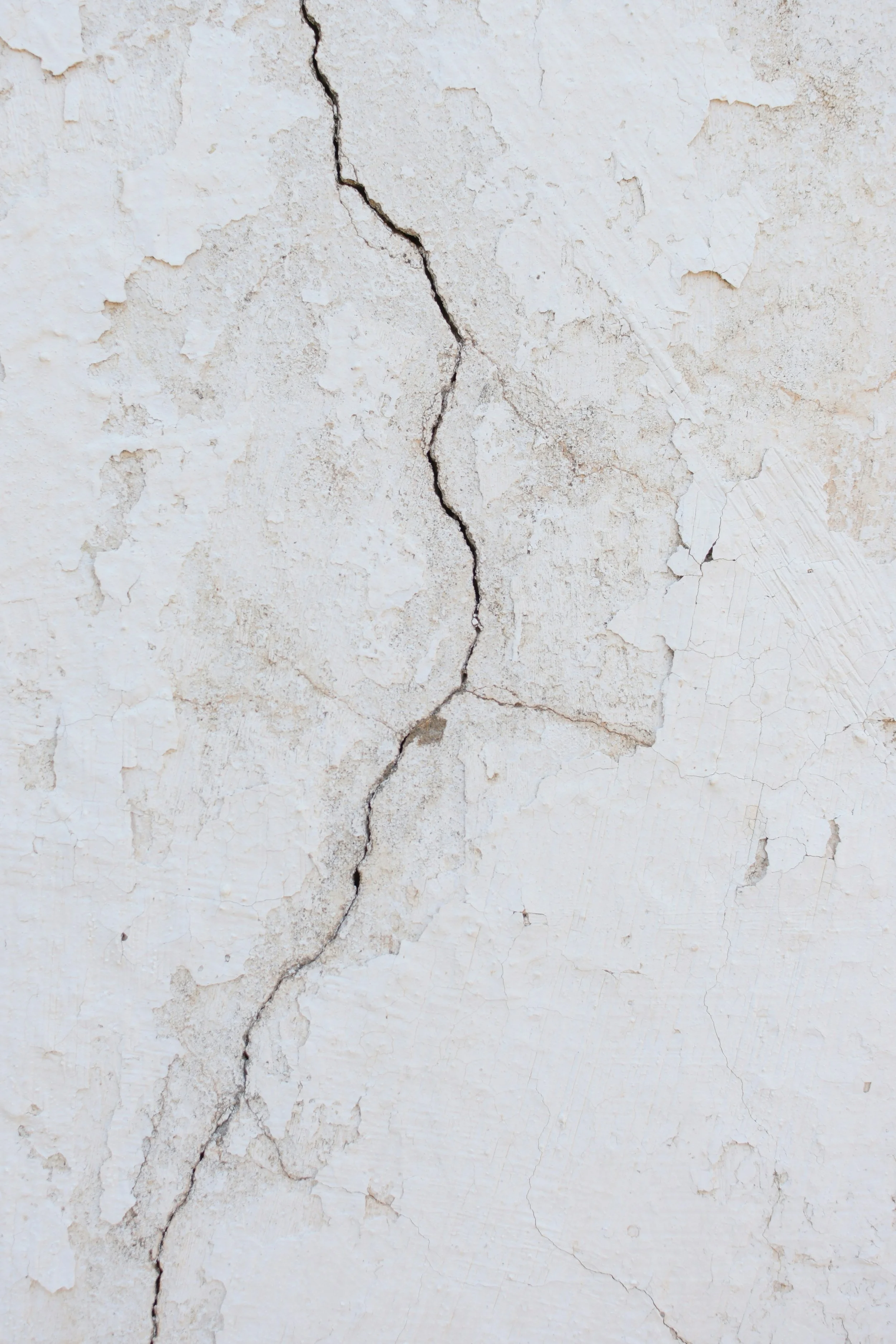 Close-up of a white wall with multiple cracks and peeling paint.