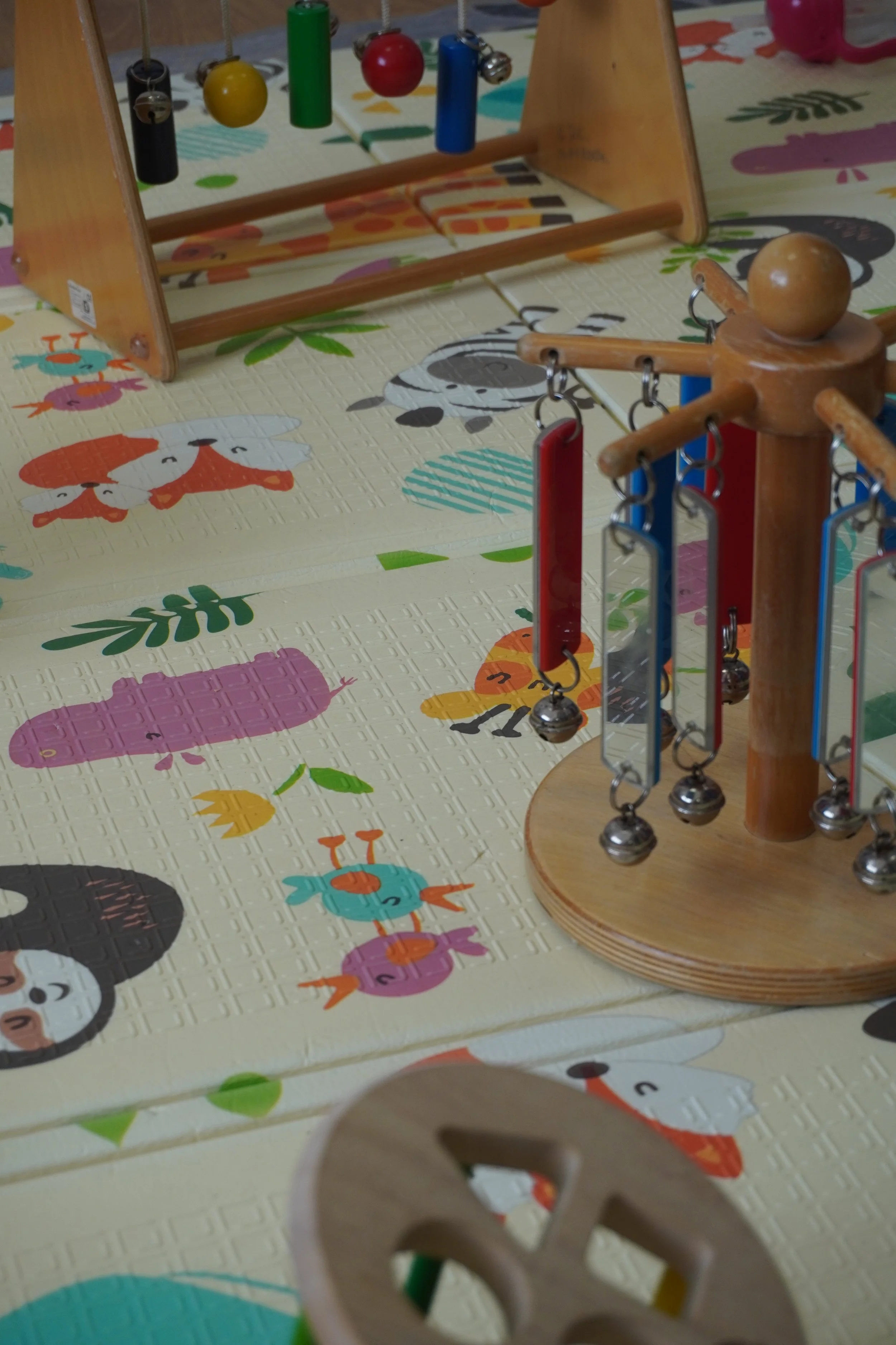 Close-up of a colorful children's activity table with animal-themed patterns, featuring a wooden and metal xylophone with hanging metal balls and colored metal bars.