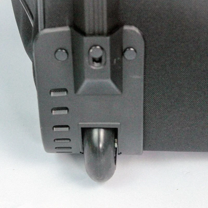 Close-up of the bottom corner of a black suitcase, showing the wheel and part of the handle mechanism.