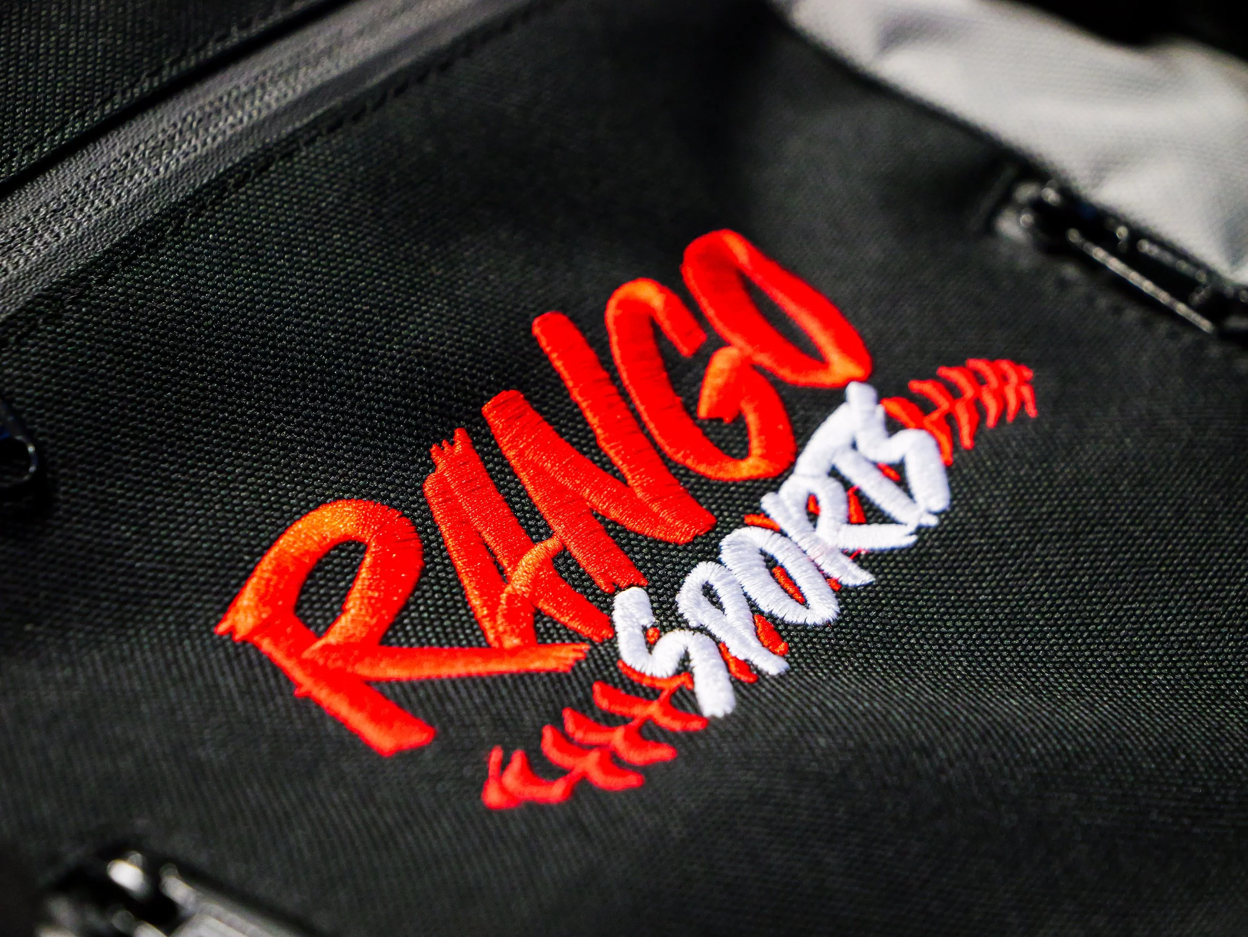 Close-up of a black backpack with embroidered red, white, and orange text and designs.