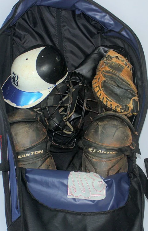 Open sports bag containing a baseball helmet, a baseball glove, and two baseballs.