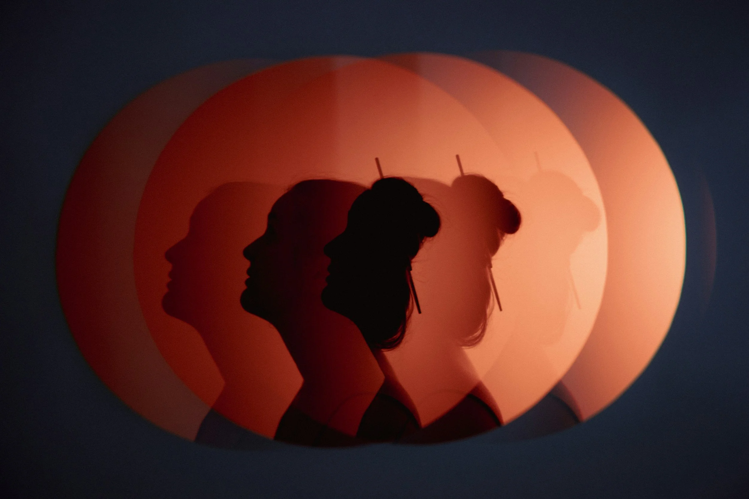 Silhouettes of a woman with a ponytail, facing left, overlaid with multiple colored circular shapes in shades of orange and red.