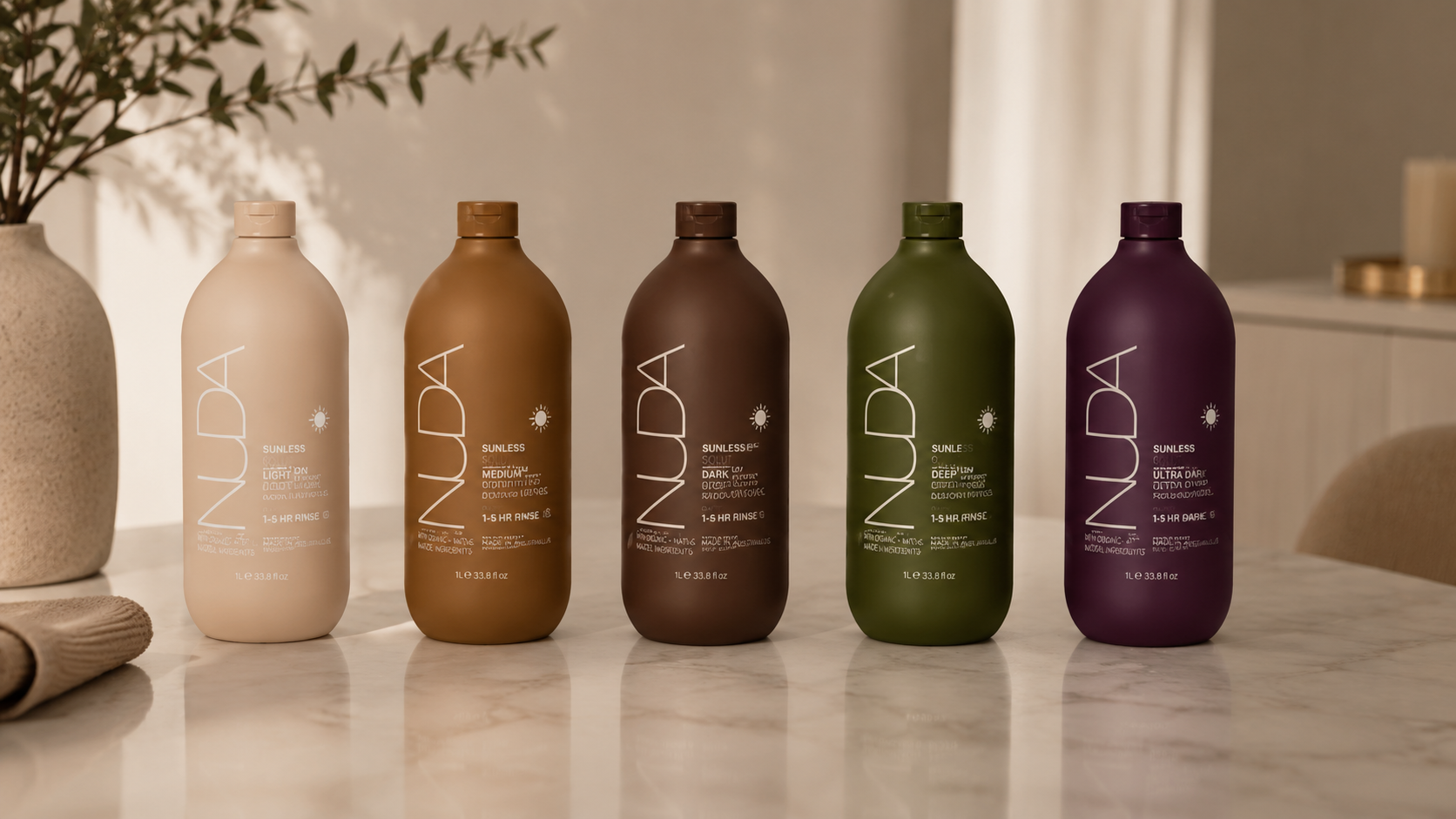 Five bottles of sunless tanning lotion in light, medium, dark, deep, and ultra dark shades, arranged in a row on a marble countertop in a well-lit room.