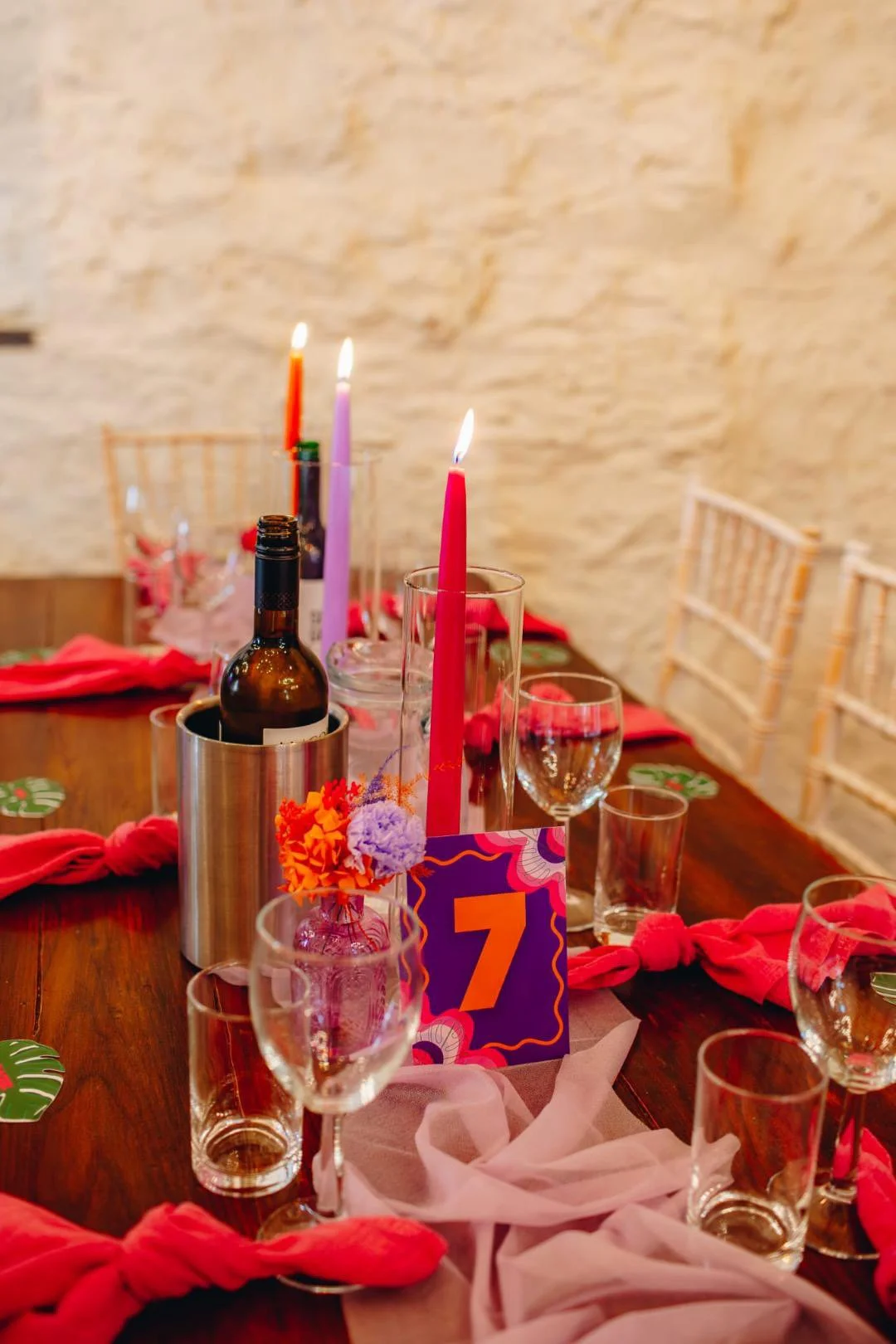Decorated dining table for a celebration with candles, glasses, a bottle, colorful flowers, and a table number '7' card.