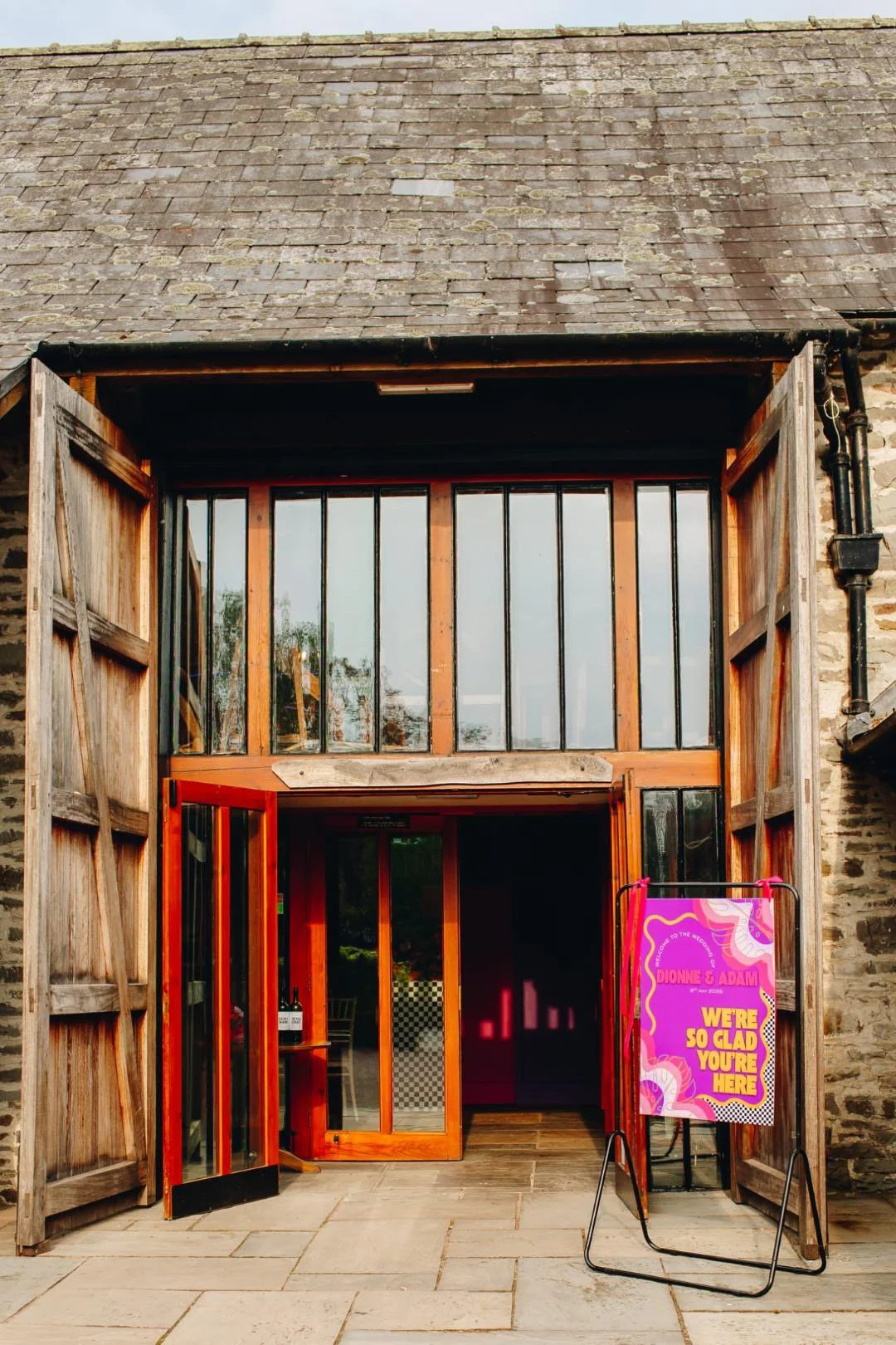 The entrance to a rustic building with large wooden shutters, glass windows, and a sign that reads: 'We're so glad you're here'.