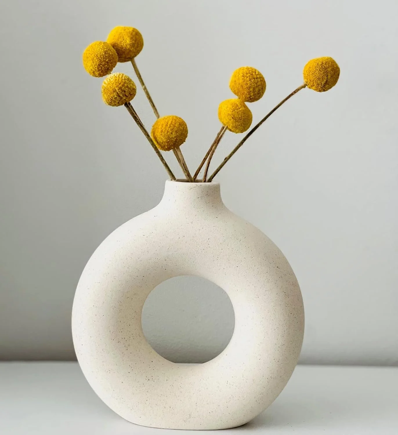 Scandi inspired modern white ceramic vase with a circular hole in the center, holding yellow billy button flowers.