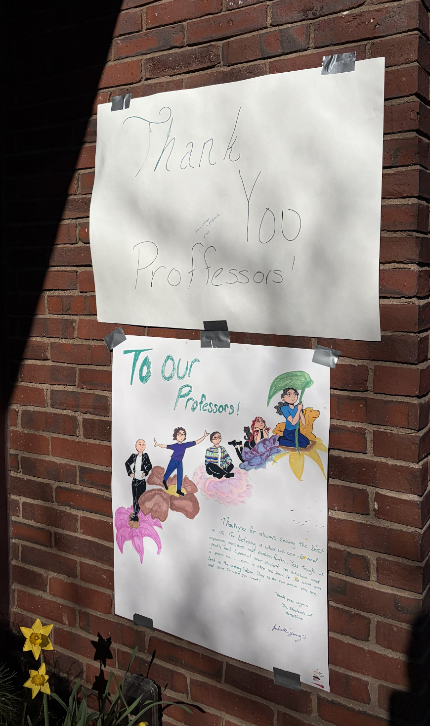 Handmade signs on a brick wall, one reading "Thank You Professors!" and the other with a colorful drawing of children and a message of appreciation for teachers.
